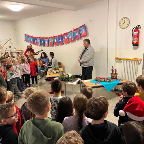 Pfarrer, Kinder und Lehrpersonen stehen um die Adventkränze herum