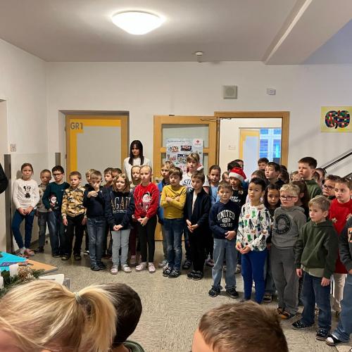 Kinder und Lehrpersonen stehen vor den Adventkränzen