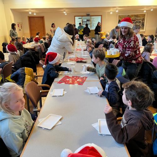 Kinder und Lehrpersonen sitzen an den Tischen und frühstücken