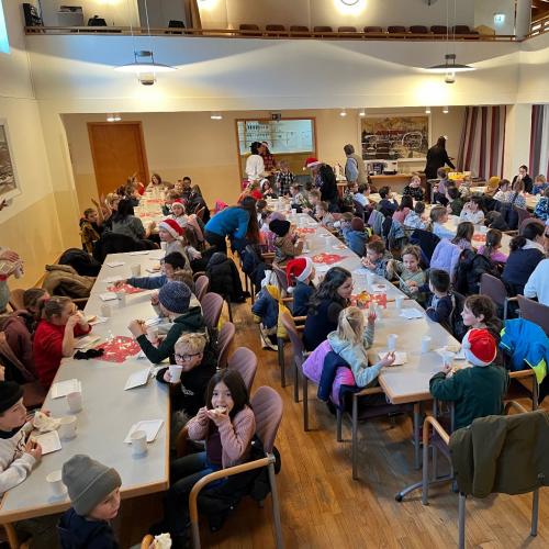 Kinder und Lehrpersonen sitzen an den Tischen und frühstücken