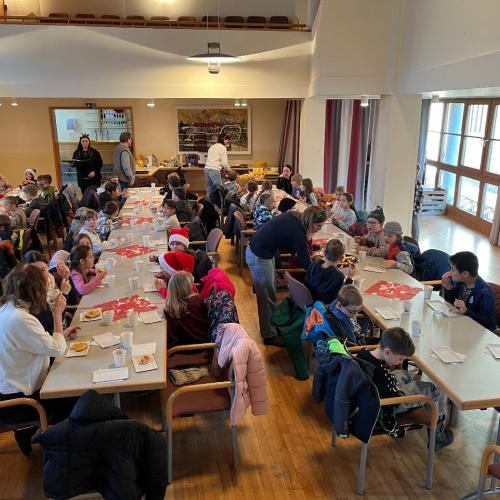 Kinder und Lehrpersonen sitzen an den Tischen und frühstücken