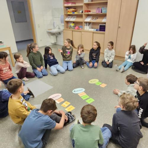 Kinder sitzen im Kreis am Boden und ordnen Wortkarten
