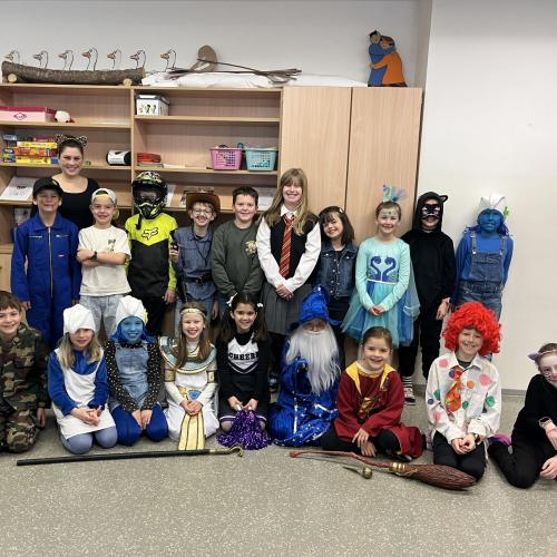 Verkleidete Kinder und Lehrerin stehen vor Regal/ sitzen am Boden