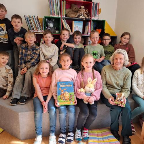Kinder der 2b Klasse sitzen mit Vorleserin auf Sitzstufen