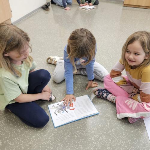 3 Kinder sitzen am Boden und lesen