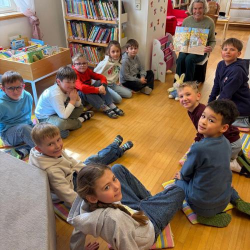 KInder sitzen im Kreis am Boden und hören der Vorleserin zu