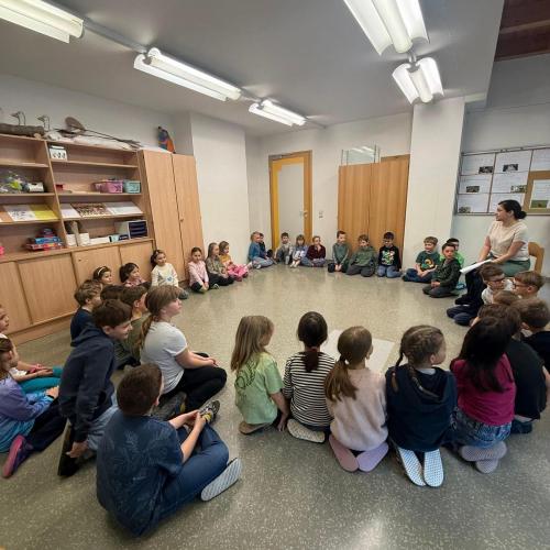 Kinder sitzen im Kreis und Lehrerin liest vor