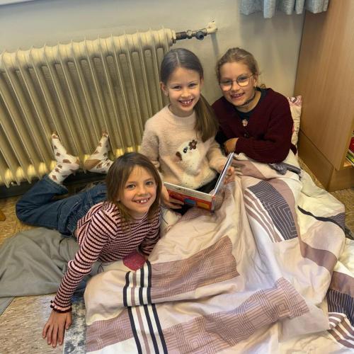 3 Kinder sitzen am Boden mit einer Decke