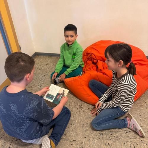3 Kinder sitzen am Boden und lesen