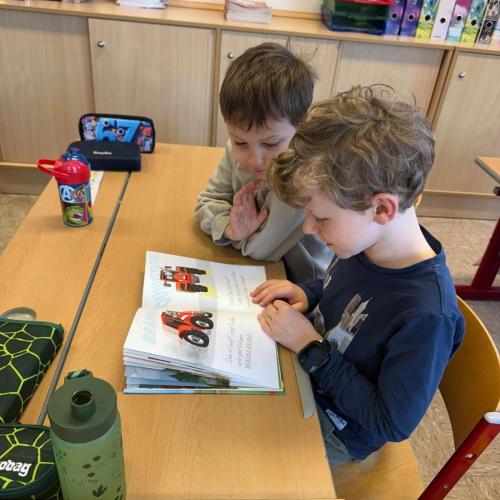 2 Kinder sitzen am Tisch und schauen Buch an
