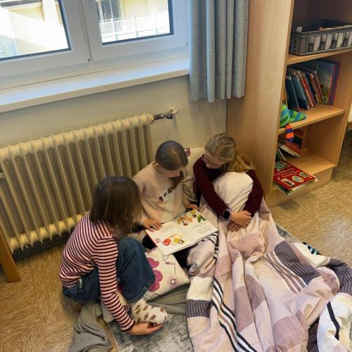 3 Kinder sitzen am Boden und lesen