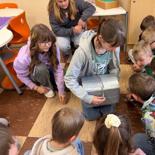 Kinder sitzen um Schülerin herum, die Schatzkiste hält
