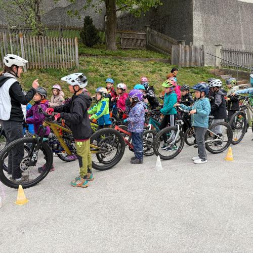 KInder stehen mit ihren Rädern in Reihen und hören der Trainerin zu