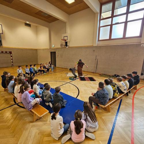 Kinder sitzen auf Bänken um die Vortragende herum