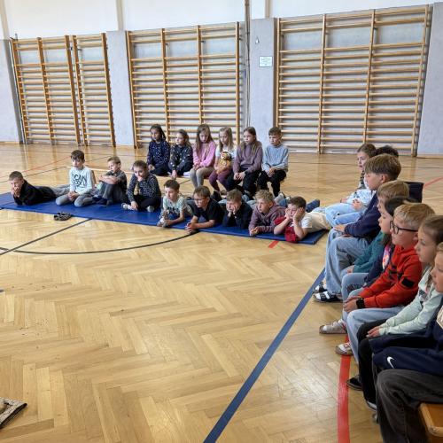 KInder sitzen auf Bänken und Matten und hören zu