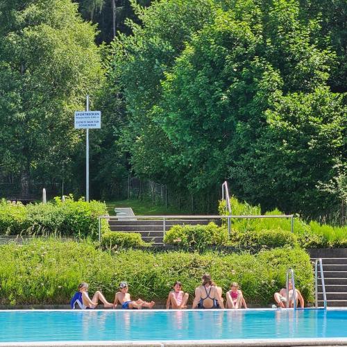 Kinder sitzen auf dem Boden am Beckenrand und machen Beinübungen