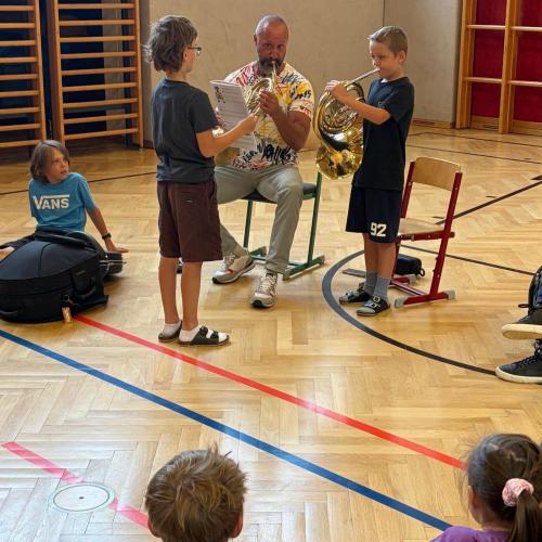 Musiklehrer und Schüler spielen auf dem Horn, ein Kind hält das Notenblatt