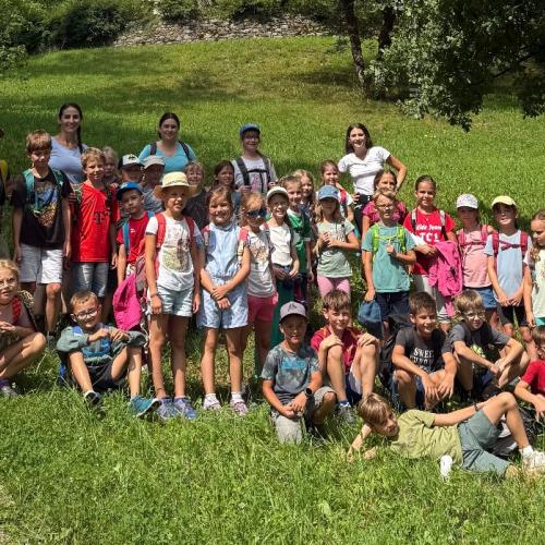 Schüler:innen und Lehrpersonen der beiden Klassen stehen/sitzen auf Wiese neben dem Schlossteich