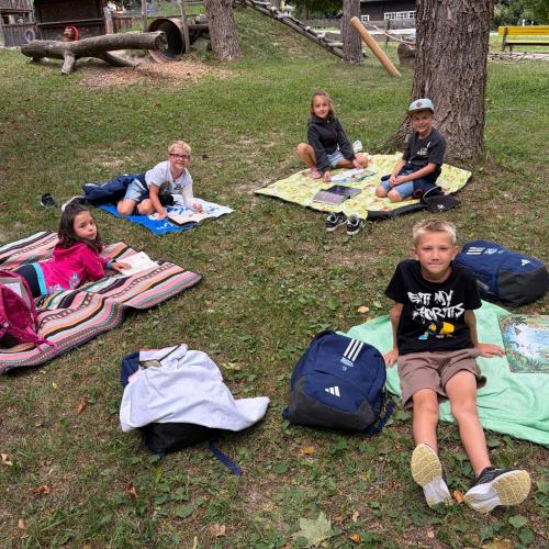 Kinder sitzen auf Decken auf der Wiese und lesen ein Buch