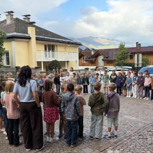 Schüler:innen und Lehrpersonen stehen im Kreis auf dem Schulplatz