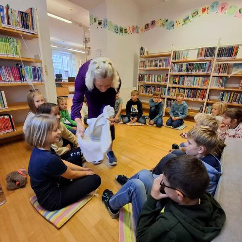 Kinder sitzen am Boden, Büchereimitarbeiterin zeigt ihnen Vamperl