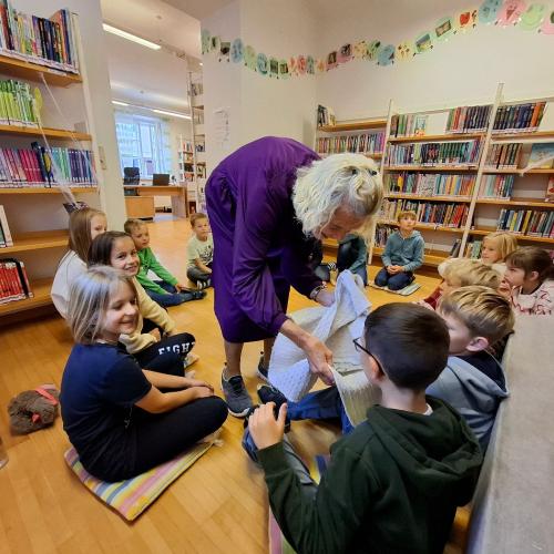 Kinder sitzen am Boden, Büchereimitarbeiterin zeigt ihnen Vamperl