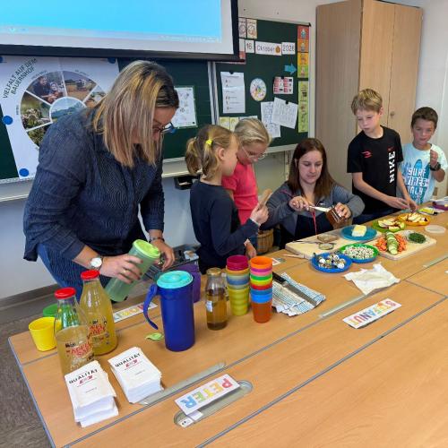 Kinder und Bäuerinnen um Tisch mit Jause, Kinder belegen Brote