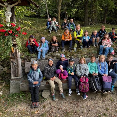 Kinder sitzen auf Bank und Wiese neben Bildstock
