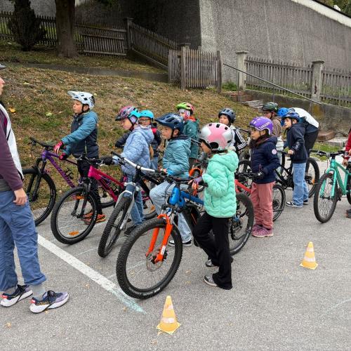 Kinder stehen mit den Rädern in der Gruppe und hören der Fahrlehrerin zu