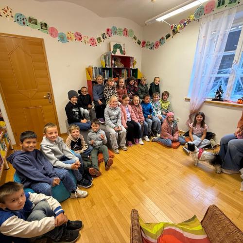 Kinder der 2a-Klasse und Büchereimitarbeiterin sitzen vor den Bücherregalen