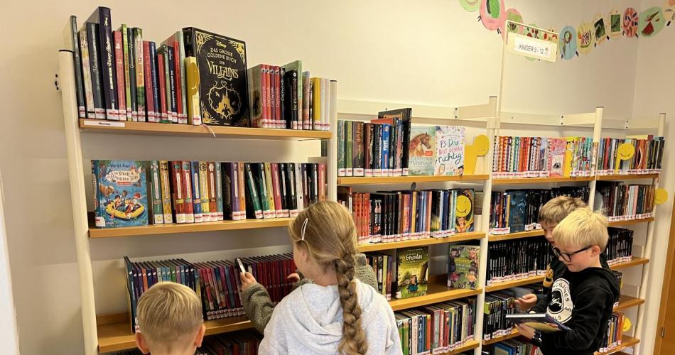 KInder stehen vor dem Bücherregal und suchen Bücher aus