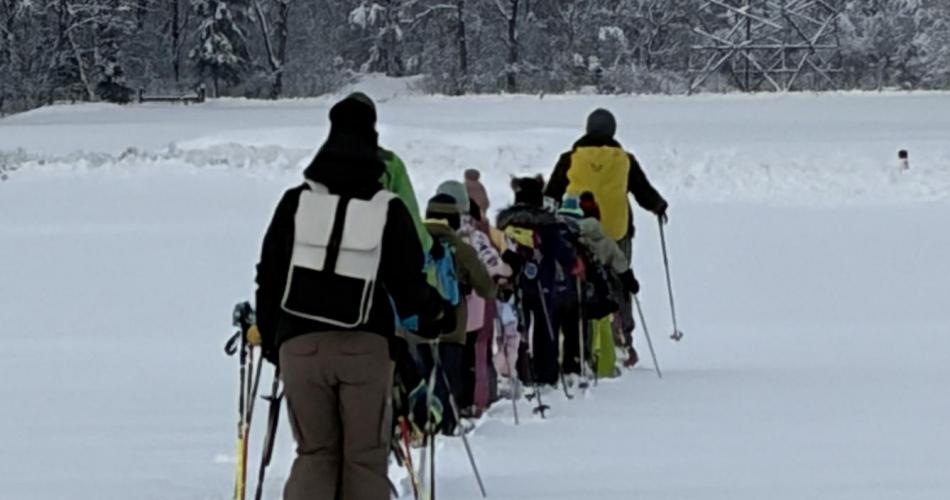 Kinder und Lehrperson gehen hintereinander mit den Schneeschuhen über das Feld