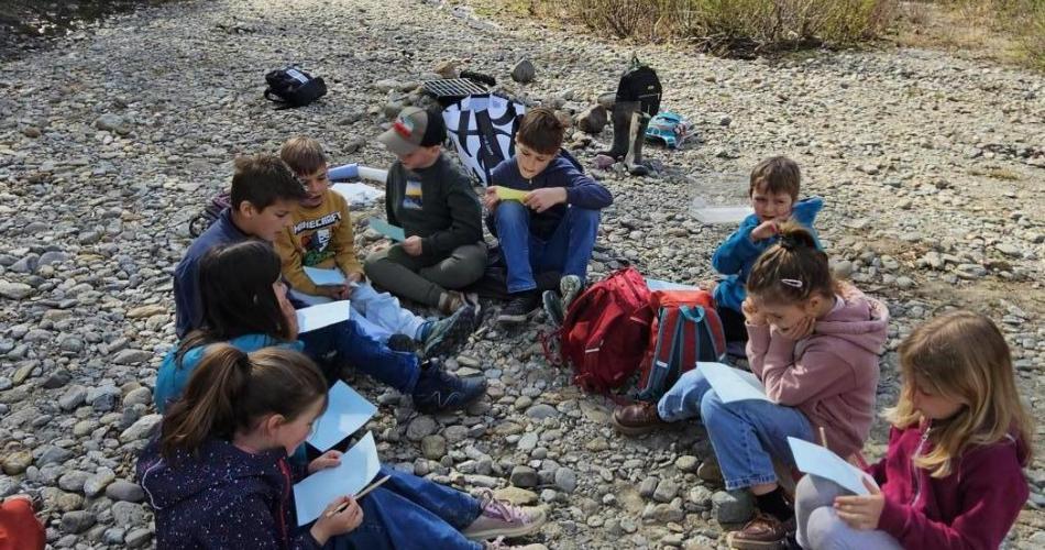 Kinder sitzen am Bach und zeichnen Tiere
