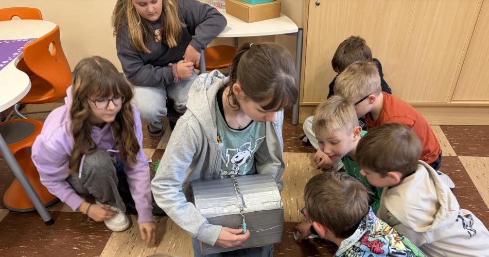 Kinder sitzen um Schülerin herum, die Schatzkiste hält