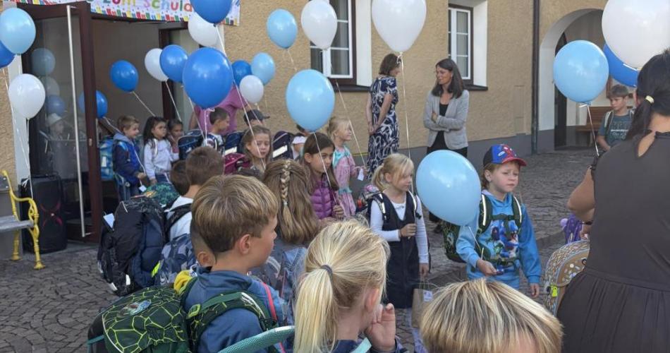 Kinder der 1. Klasse kommen mit Luftballons aus dem Schulhaus