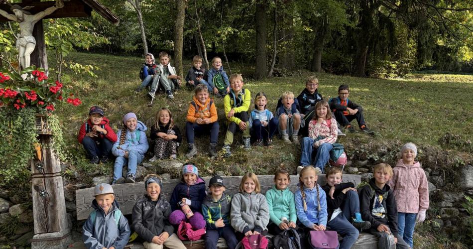KInder sitzen auf Bank und Wiese neben Bildstock