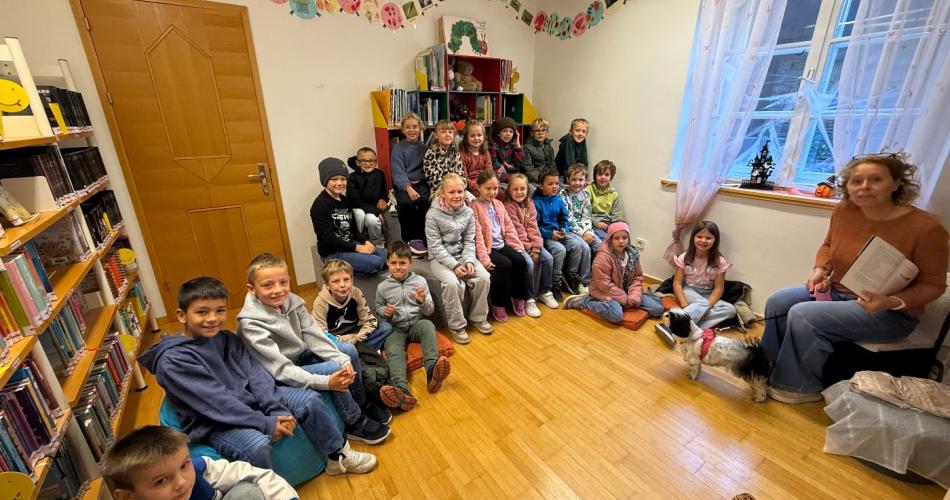 Kinder der 2a-Klasse und Büchereimitarbeiterin sitzen vor den Bücherregalen